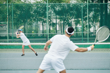 Smiling young woman hitting ball with racket when playing tennis with boyfriend outdoors