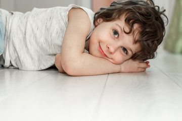 curly boy lying on white floor at home and smiling. the concept of underfloor heating, quality lamin