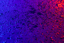 Drops Of Water On A Textural Surface In Neon Light. Reflection Of Red-blue Light In Drops Of Water. Dark Photo.