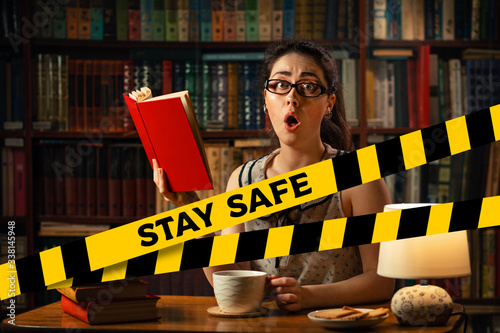 Do not cross.Barrier tape-quarantine,isolation.A young woman with glasses reads a book with surprise,holding a Cup of tea in her hands.The concept of self-isolation, distance learning and remote work