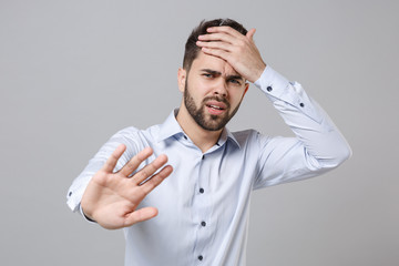 Canvas Print - Puzzled young unshaven business man in light shirt posing isolated on grey background. Achievement career wealth business concept. Mock up copy space. Showing stop gesture with palm, put hand on head.