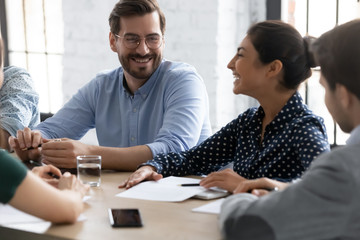 Wall Mural - Smiling diverse businesspeople gather at desk in office have fun joke discussing ideas together, happy multiethnic colleagues laugh negotiate brainstorming at meeting in boardroom, teamwork concept