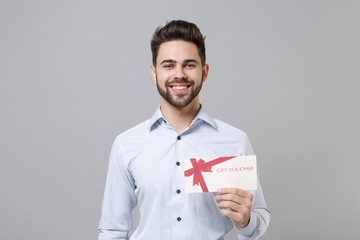 Canvas Print - Smiling young unshaven business man in light shirt posing isolated on grey wall background studio portrait. Achievement career wealth business concept. Mock up copy space. Holding gift certificate.