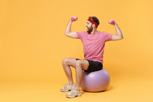 Funny Young Bearded Fitness Sporty Guy Sportsman In Headband T-shirt In Home Gym Isolated On Yellow Background. Workout Sport Motivation Lifestyle Concept. Sit On Fitball Doing Exercise With Dumbbell.