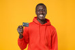 © ViDi Studio - Smiling young african american man guy in red streetwear hoodie posing isolated on yellow wall background studio portrait. People emotions lifestyle concept. Mock up copy space. Hold credit bank card.