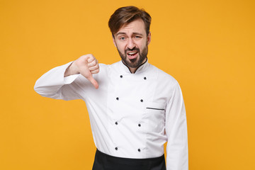 Wall Mural - Dissatisfied young bearded male chef cook or baker man in white uniform shirt posing isolated on yellow wall background studio portrait. Cooking food concept. Mock up copy space. Showing thumb down.