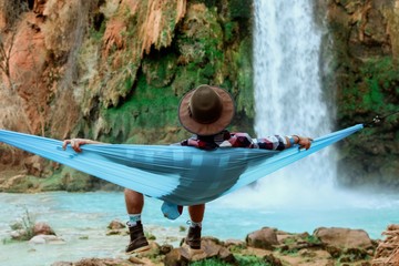 Wall Mural - rear view of man relaxing in hammock by waterfall