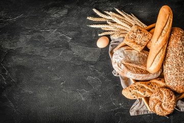 Poster - Fresh bakery food, rustic crusty loaves of bread and buns on black stone background. Top view and copy space for text.