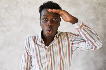 Wall Mural - Surprise, astonishment, amazement and shock concept. Picture of emotional young African guy posing isolated with hand on his head, looking into distance, sees something curious, gasping, saying Wow