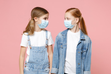 Two little kid girls 12-13 years old in sterile face mask isolated on pink background children portrait. Epidemic pandemic coronavirus 2019-ncov sars covid-19 flu virus concept. Looking at each other.