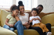 © fizkes - African american smiling family with two children having good time using smartphone. Young happy diverse husband and wife with cute daughter and son using applications in mobile phone.
