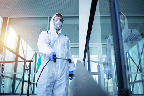 Fotomural Shot of male person in white chemical protection suit doing disinfection of public areas to stop spreading highly contagious corona virus