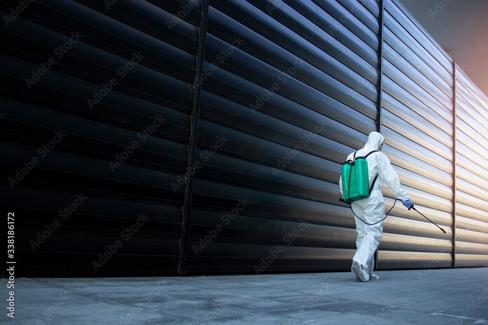 Shot of male person in white chemical protection suit doing disinfection of public areas to stop spreading highly contagious corona virus. Stop coronavirus or COVID-19. - obrazy, fototapety, plakaty 