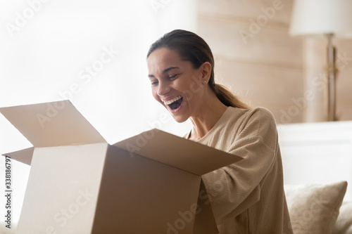 Fotomural Excited young woman unpacking huge carton box, looking inside
