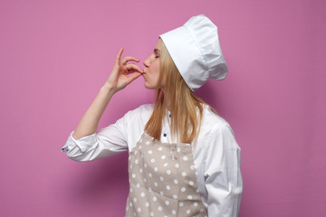 cheerful girl cook in kitchen clothes shows a belissimo gesture on a colored background, a woman housewife shows a sign of good taste