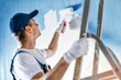 Painter painting a wall with paint roller. Builder worker painting blue surface with white color