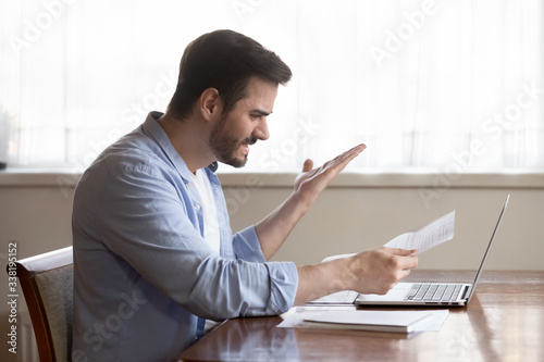 Fotomural Angry young man holding paper letter, irritated by bad news banking debt notification, sitting at table with computer at home