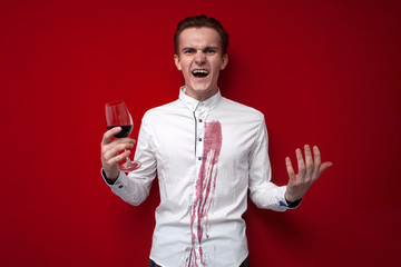 sad guy in a white shirt spilled red wine on himself on a red background, an angry man put a stain of wine on his clothes