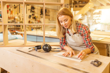 attractive caucasian carpenter lady deals with drawings during work, woman use pencil and ruler before making wooden furniture in workshop