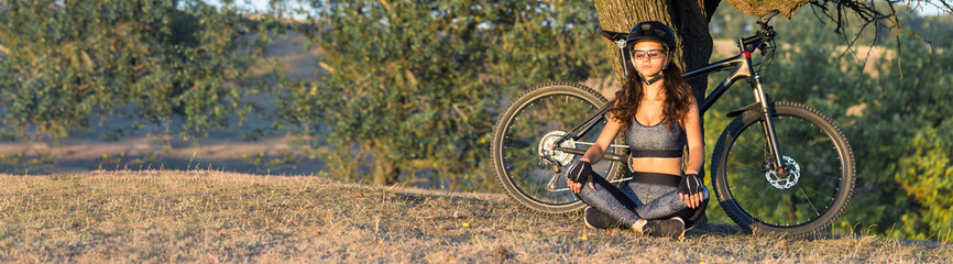 Girl on a mountain bike on offroad, beautiful portrait of a cyclist at sunset, Fitness girl rides a modern carbon fiber mountain bike in sportswear. Close-up portrait of a girl in a helmet and glasses