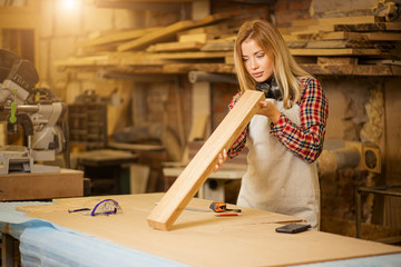 portrait of beautiful caucasian woman carpenter dealing with handicraft, woman has own business connected with making wooden furniture in workshop