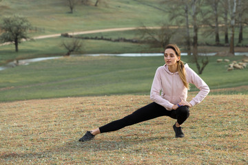 A young slim athletic girl in sportswear performs a set of exercises. Fitness and healthy lifestyle  against the background of green spring pasture hills.