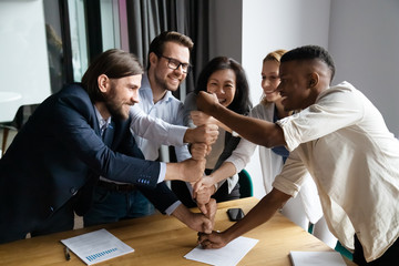 Overjoyed diverse multiethnic businesspeople stack fists motivated for shared success or goal achievement, excited multiracial colleagues engaged in motivational teambuilding activity at meeting