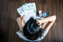 Top View Of Stressed Young Asian Woman Hands Holding The Head Trying To Find Money To Pay Credit Card Debt And All Loan Bills. Financial Problem From Coronavirus Or Covid-19 Outbreak Crisis Concept.