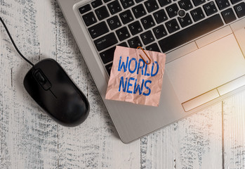 Poster - Writing note showing World News. Business concept for global noteworthy information about recent or important events Trendy metallic laptop crushed colored paper note pen on wooden table