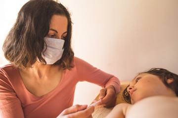 Wall Mural - A woman in a protective mask measures the temperature of the child.