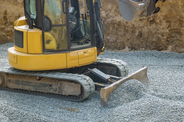 Excavator with a bucket lowered down gravel stones for construction of foundation