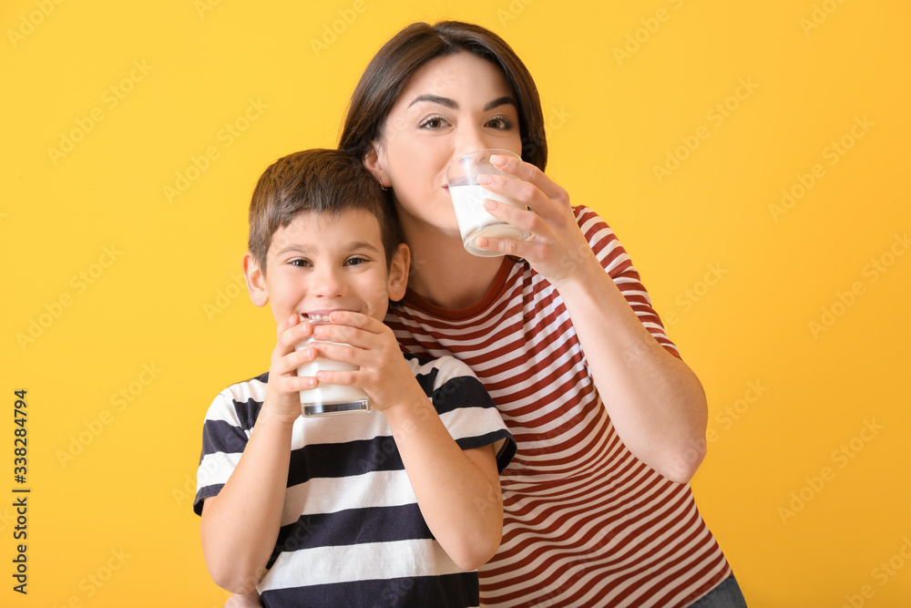 Mother with her little son drinking milk on color background