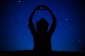 Wall Mural - silhouette of a girl holding heart-shape symbol for love on a starry night sky. my astronomy work.