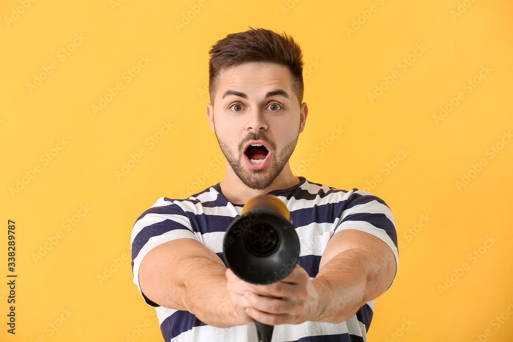 Surprised young man with blow dryer on color background