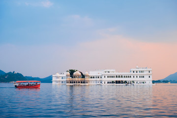 Fototapete - Romantic luxury India travel tourism - tourist boat in front of Lake Palace (Jag Niwas) complex on Lake Pichola on sunset with dramatic sky, Udaipur, Rajasthan, India