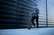 Businessman on his way to work. Young elegant man walking with electric scooter and using smart phone or texting message..