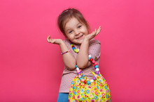 Studio Shot Of Cute Charming Little Lady Wearing Casual Outfit And Different Multicolored Jewelry, Keeping Hands Near Face, Looking Smiling Directly At Camera, Having Funny Facial Expression.