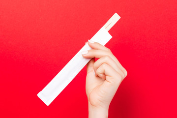 Wall Mural - Woman's hand holding chopsticks in a pack on red background. Chinese food concept with empty space for your design