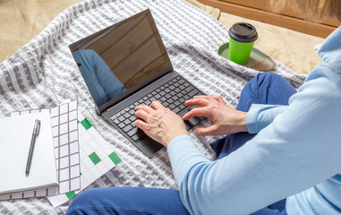 Woman working for laptop from home on bed. Girl using portable computer for writing on keyboard at her office with cup of coffee