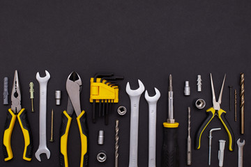 DIY Tool For Building Or Repairing On A Black Background. The Workplace Of The Foreman. Professional Repair And Construction Tool. Space For Text. Screwdriver, interchangeable nozzles, wrench, pliers.