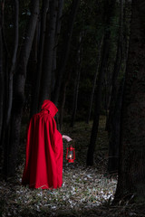 Attractive woman dressed a little red riding-hood walk in a dark forest with lantern