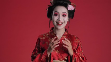 Canvas Print - A surprised young geisha woman in traditional japanese kimono is rejoicing standing isolated over red background