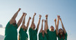© Creadores de video - Group of happy young people in green T-shirts raise their hands up and show thumbs up, on the background of blue sky in yellow grass.
