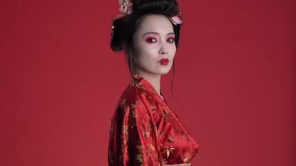 Poster - An amazing beautiful young geisha woman in traditional japanese kimono is posing while turning around isolated over red background