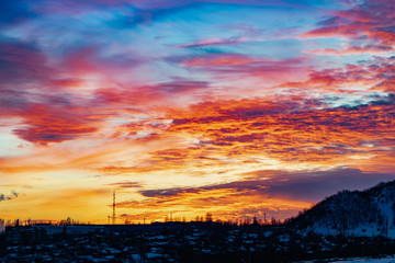 The colorful sky at sunset on a clear day plays with several colors , contrasting and rich beautiful view of the glow near the mountain and the city in winter