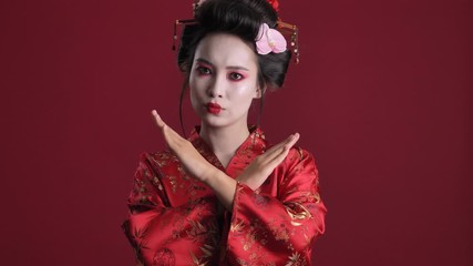 Poster - A strictly young geisha woman in traditional japanese kimono is crossing her arms while saying NO isolated over red background