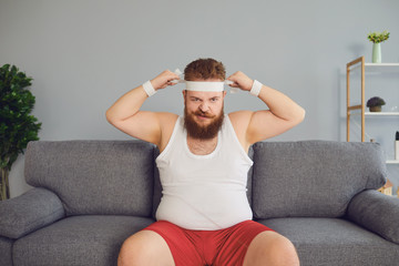 Funny fat man in sportswear is sitting on the sofa in the room