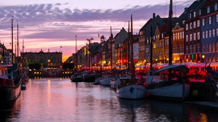 Wall Mural - Copenhagen, Denmark. Time-lapse at sunset. View of famous Nyhavn area in the center of Copenhagen, Denmark. Various boats moored with historical buildings and cloudy sunset bright sky