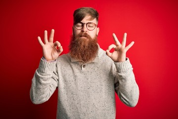 Poster - Handsome Irish redhead man with beard wearing casual sweater and glasses over red background relaxed and smiling with eyes closed doing meditation gesture with fingers. Yoga concept.