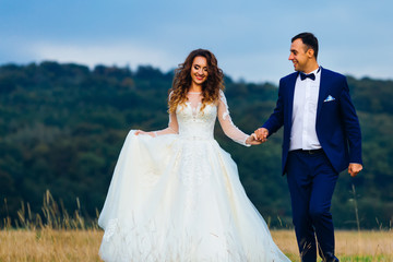 Wall Mural - happy newlyweds hold hands and walk near the forest